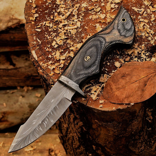 Audie Hunter handmade hunting knife resting diagonally on a wood stump with Feather Damascus blade visible.